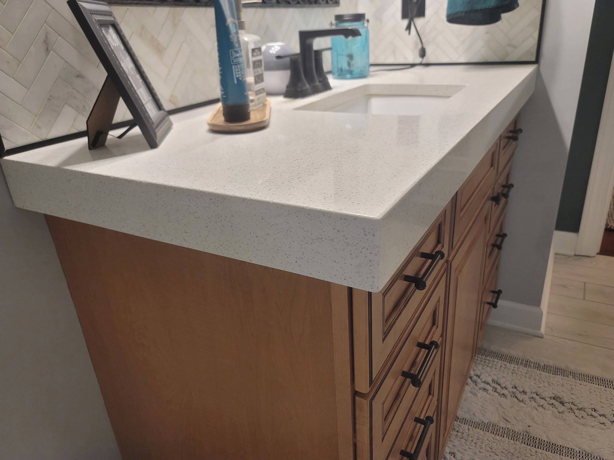 A bathroom vanity with a thick, light speckled countertop, undermount sink and wood drawers with black pulls.