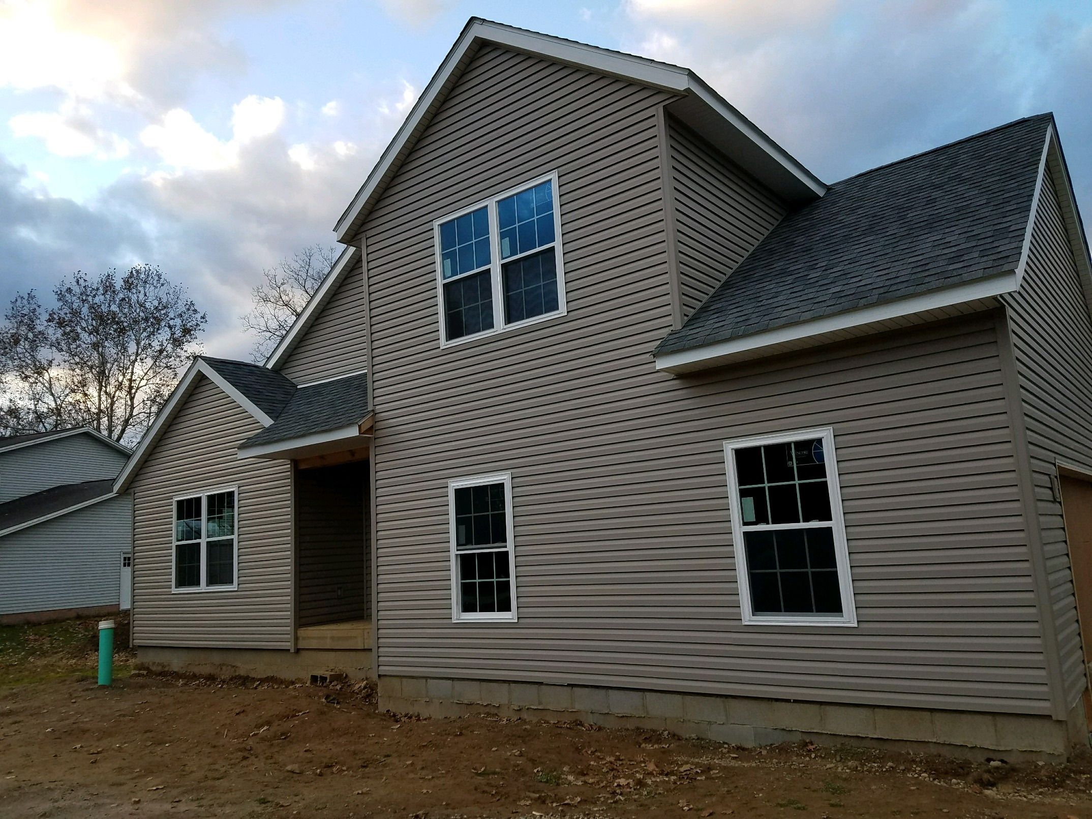 Newly built two-story home with gray vinyl siding, dark shingle roof and white-trimmed windows.