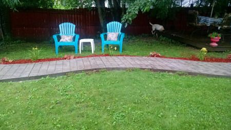 Curved paver walkway along a mulched bed with two lawn chairs.