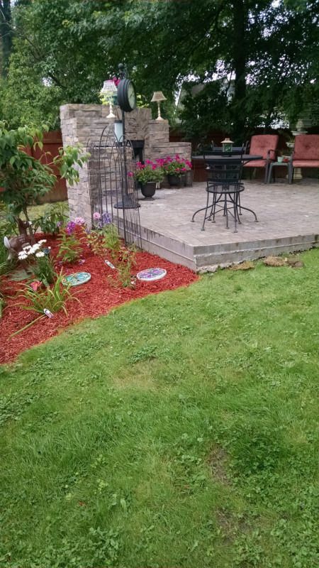 Side view of the raised paver patio with a stone pillar and mulched garden bed.