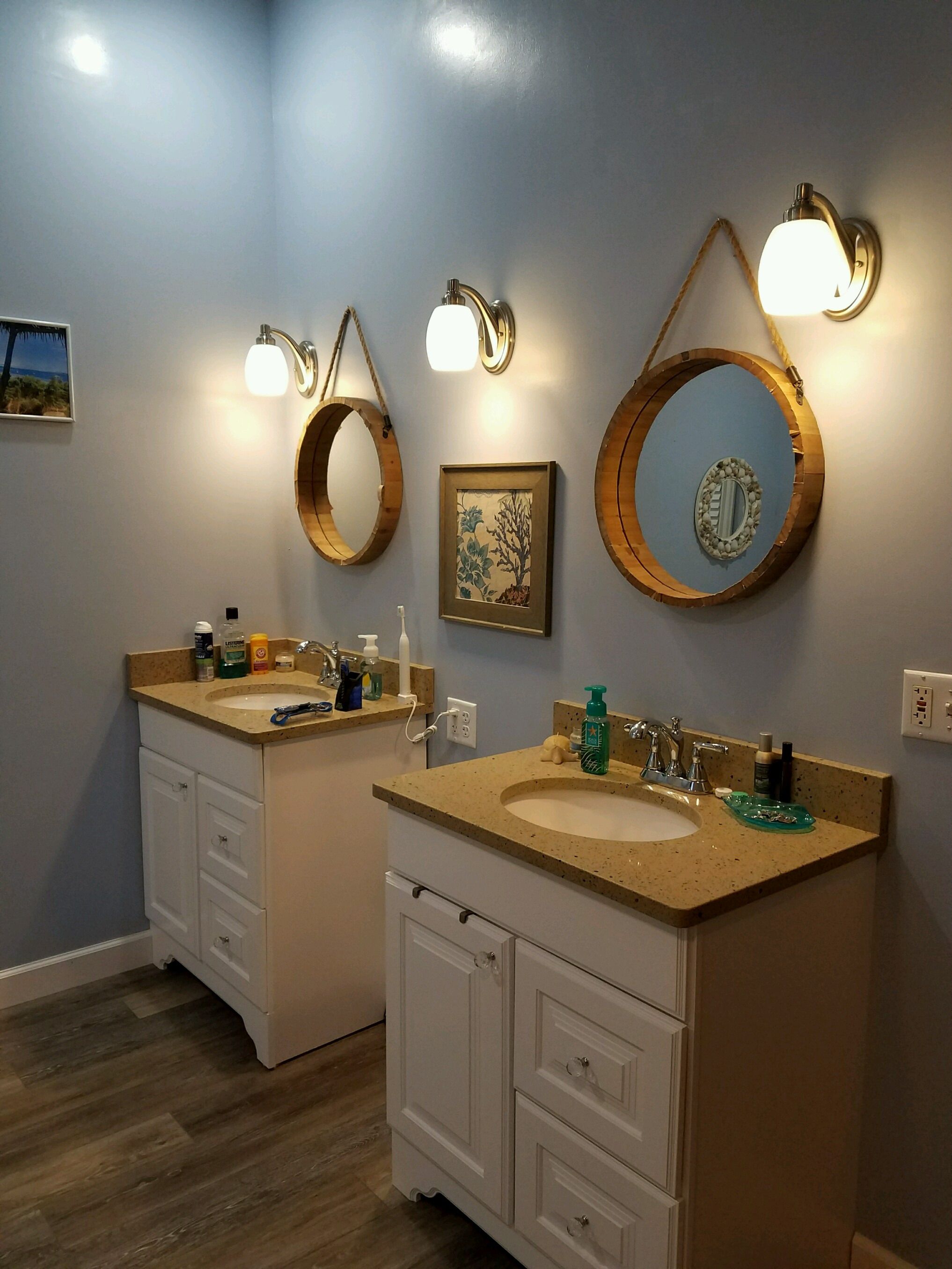 Remodeled bathroom with two white vanities, round wood-framed mirrors and wall sconces.